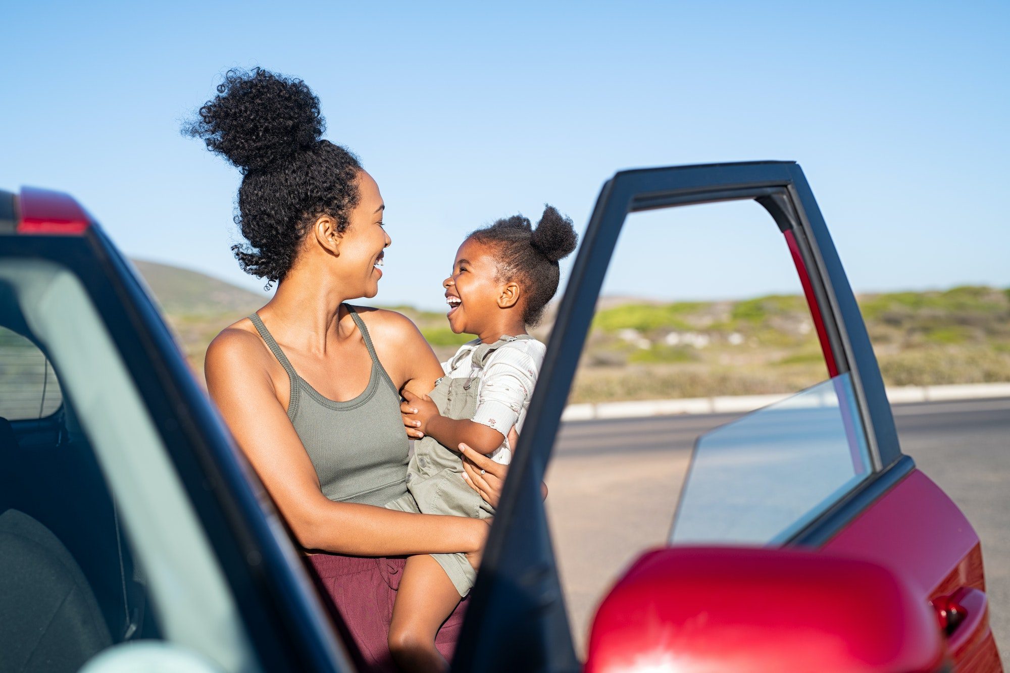 Happy black mother holding little daughter outside car