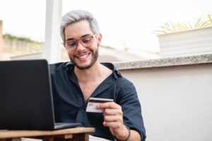 Young hipster man holding credit cart using computer laptop for online payment - E-commerce, bank