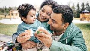 Happy family with a young child playing with letter blocks while enjoying a sunny day in the park