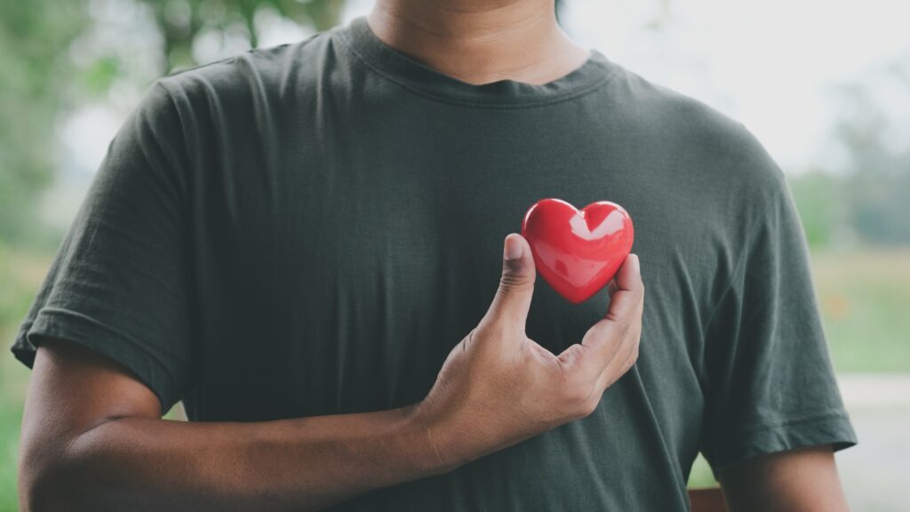 young man holding a red heart to his chest representing health importance
